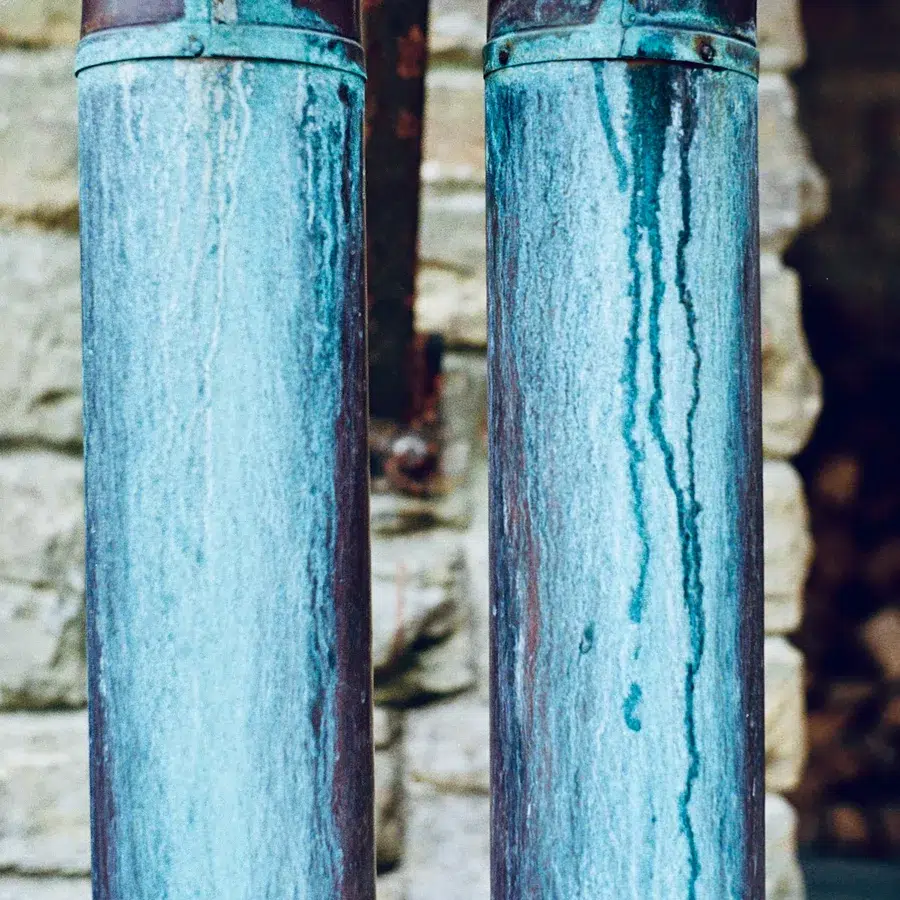 Two copper downpipes streaked blue-green against a stone wall
