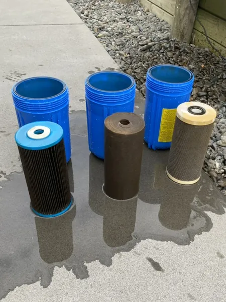 Three dirty water filter cartridges and their blue filter housings on a path after a 12-month UV service at a home in Coatesville