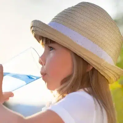 A young girl in a straw hat drinking a glass of water