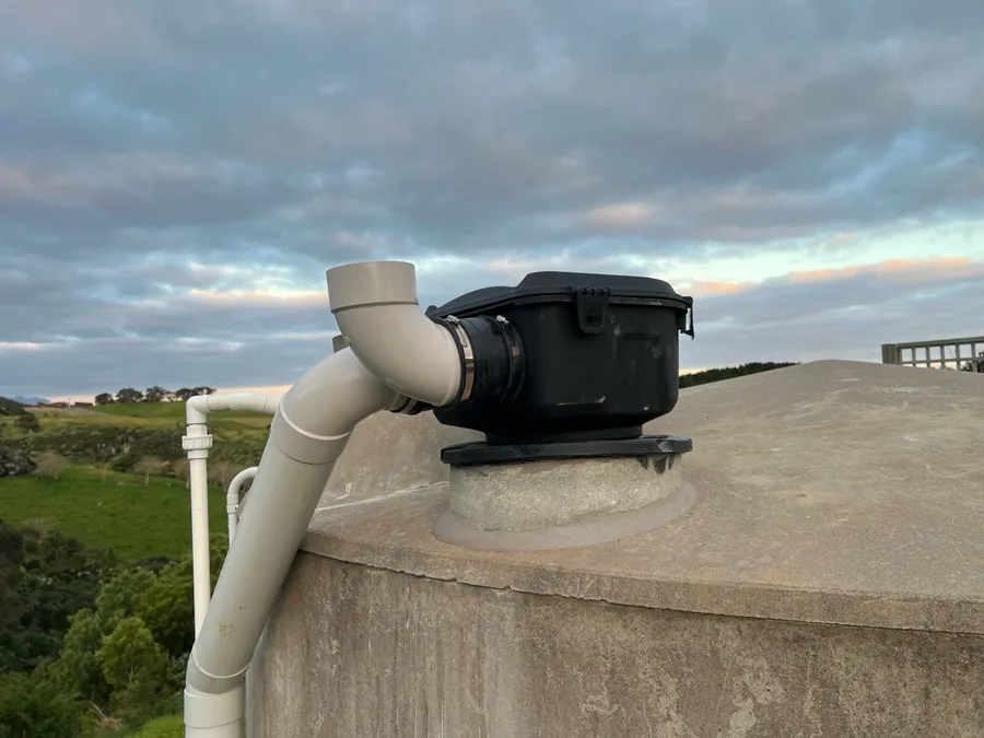 Maelstrom pre-tank filter on top of a concrete water tank at a Leigh home, with the downpipe running into it