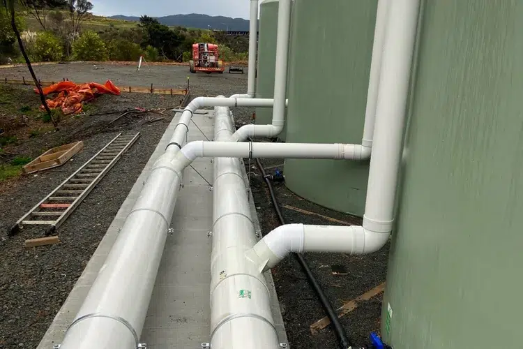 Row of large rainwater tanks with white collection pipes at a new commercial building