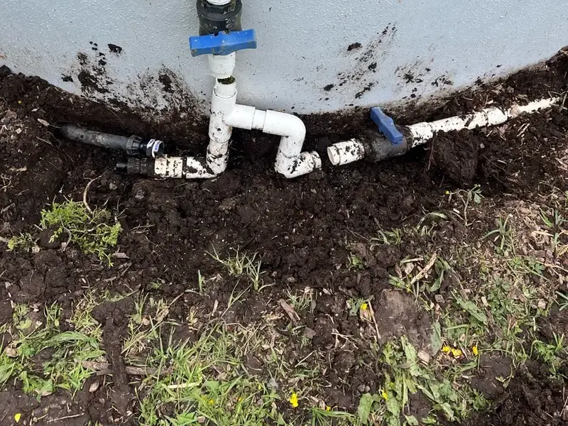 Repaired water pump suction line and new valves at the base of a concrete water tank in Redvale